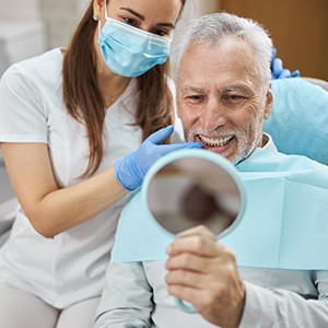 An older man admiring his new dental implants in a hand mirror