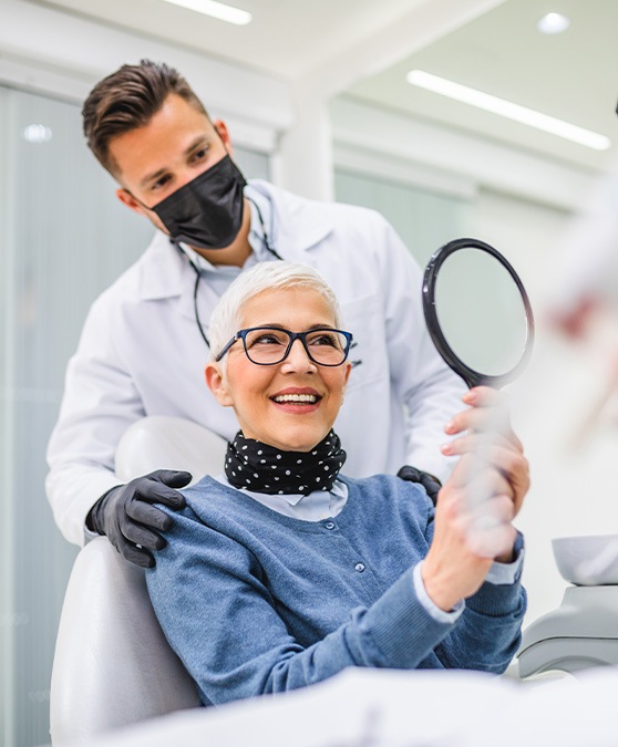 A senior woman admiring her new dental implant alongside her dentist