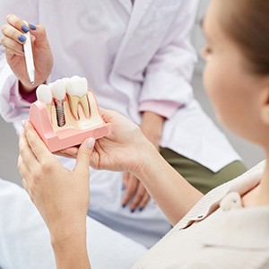 A patient holding an enlarged dental implant model while a dentist explains things