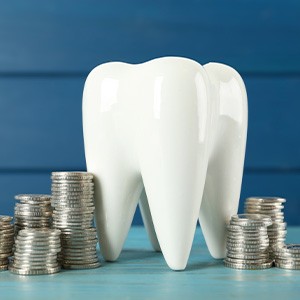 A ceramic tooth model and coins on a light blue wooden table