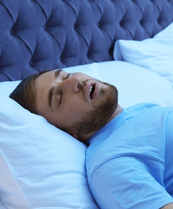 Man in blue shirt lying in bed and snoring