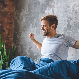 Man in grey shirt stretching in bed