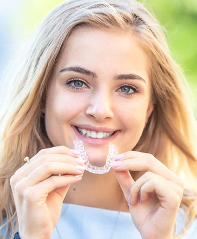 young woman smiling while holding clear aligners