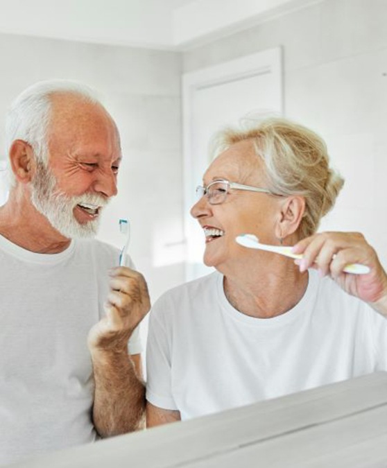 Happy older couple brushing their teeth in front of bathroom mirror