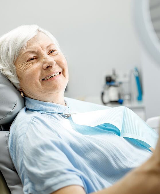 Senior woman sitting in dental chair and checking smile in mirror