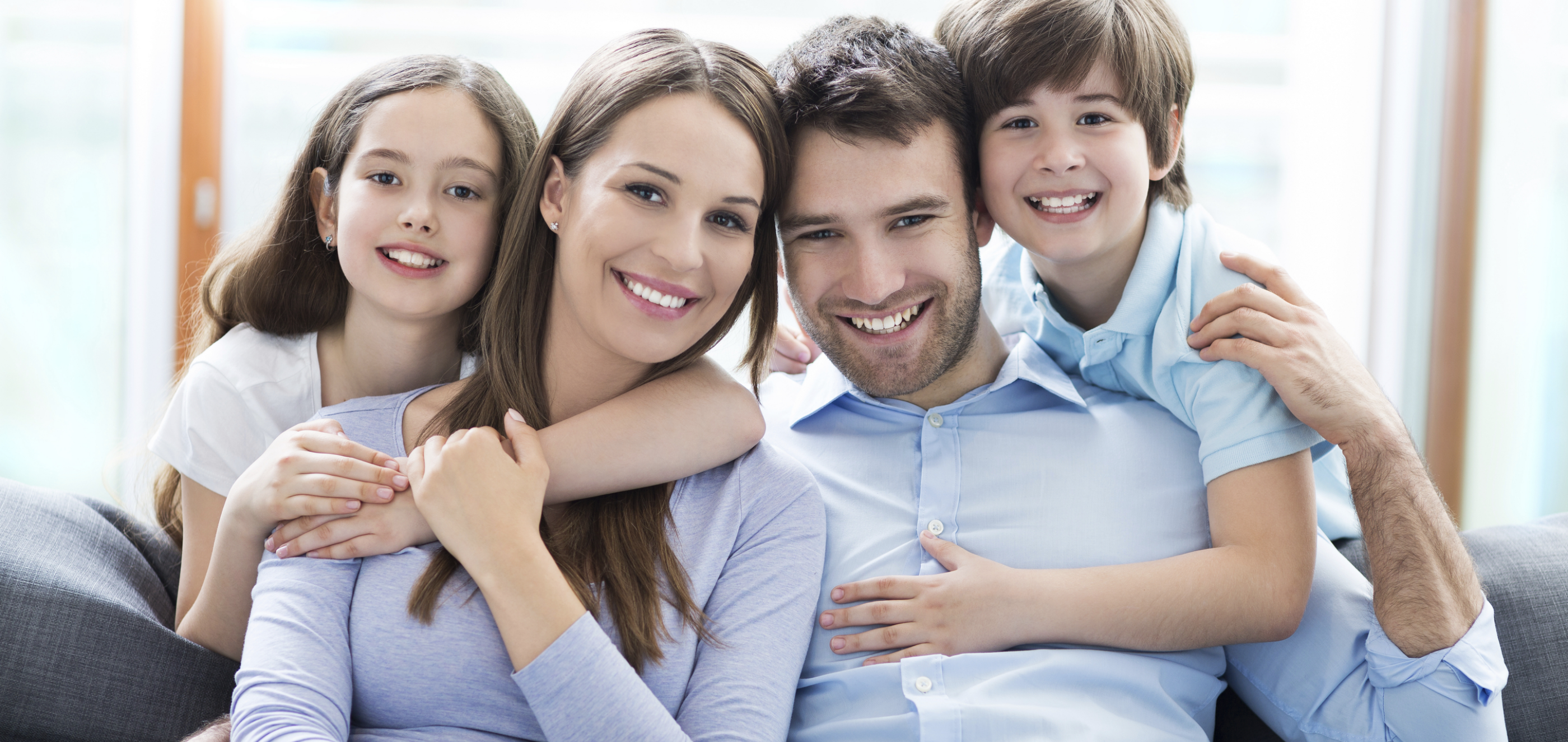 A smiling family of four sits closely together on a couch, sharing affection and joy.