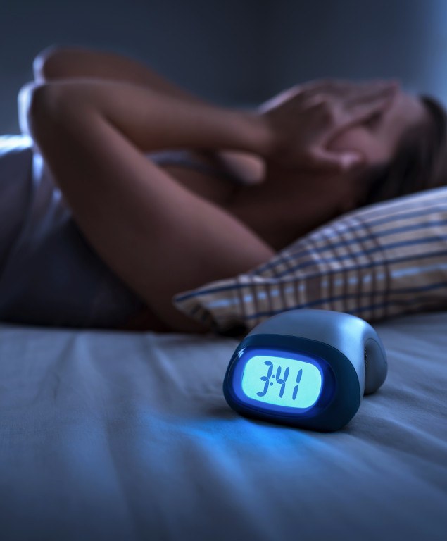 Woman lying awake in bed with alarm clock